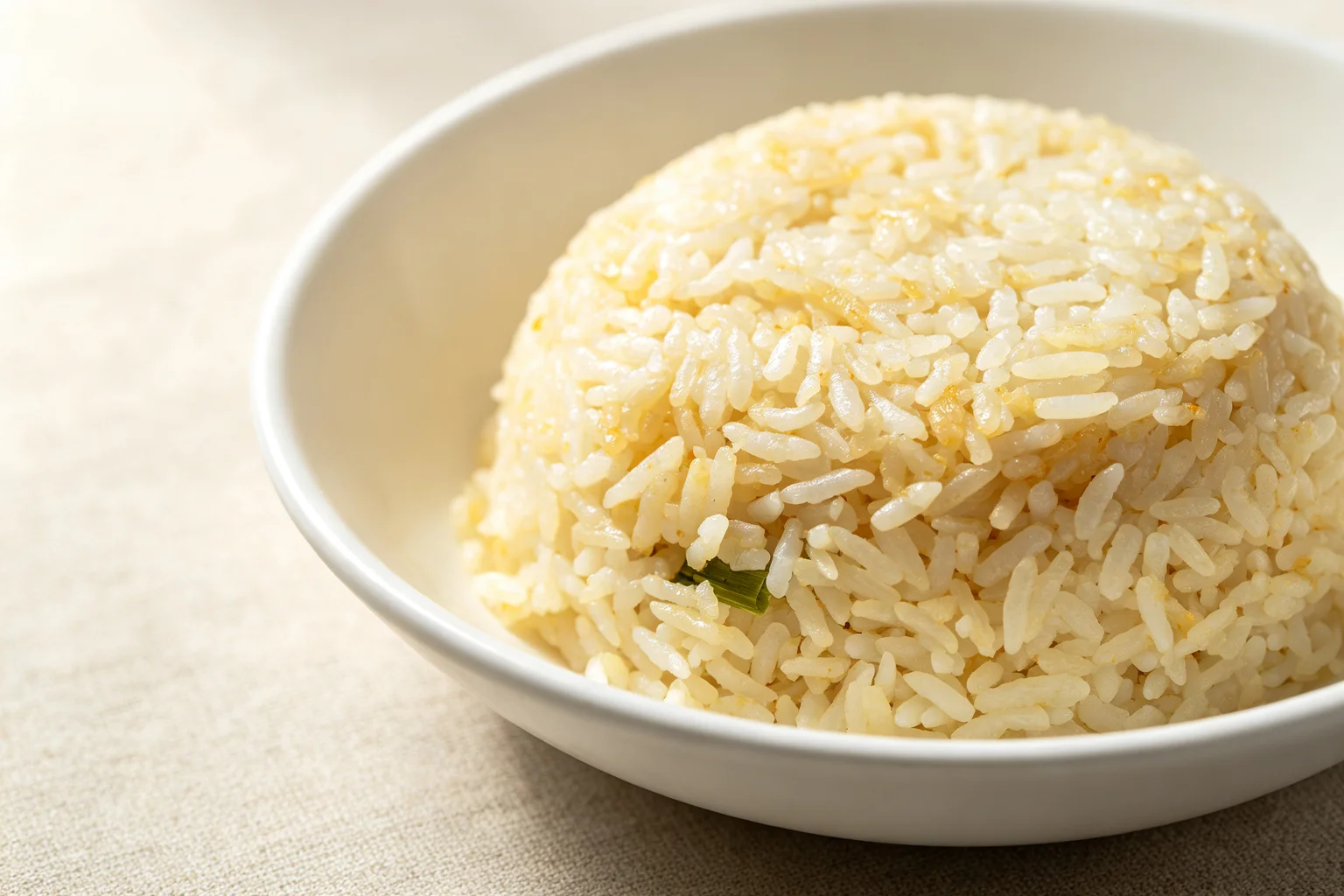 Close-up of Hainanese chicken rice showing distinct separate jasmine rice grains with a golden sheen from rendered chicken fat and pandan leaf in a white ceramic bowl