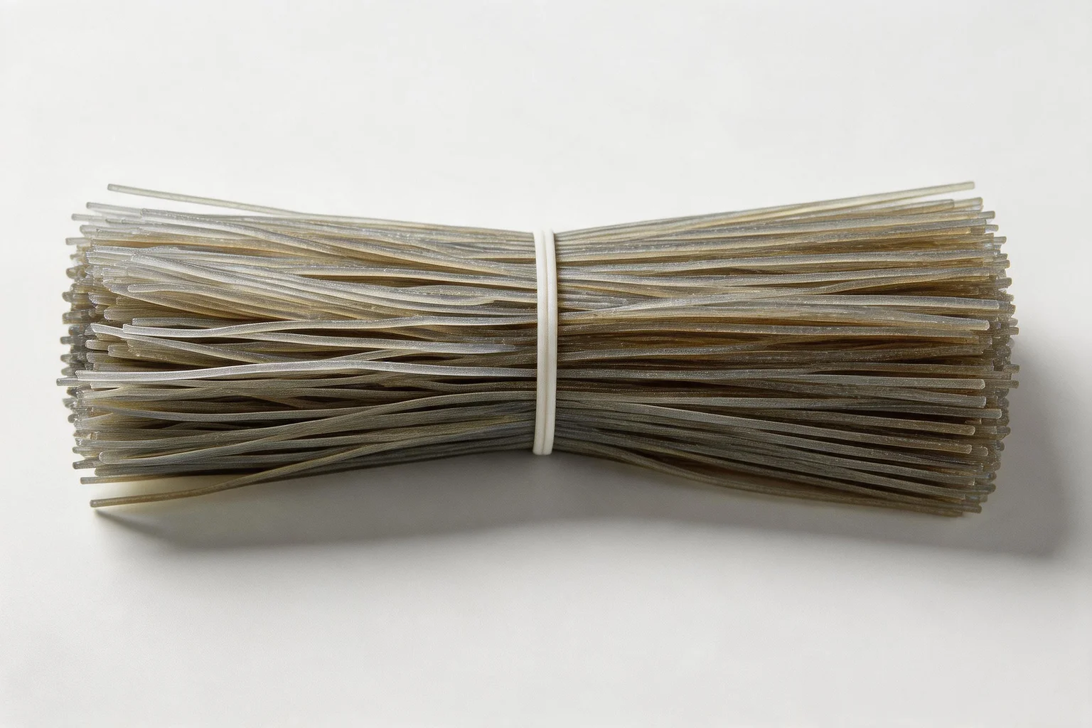 Overhead view of dry uncooked dangmyeon Korean sweet potato glass noodles bundle showing semi-transparent grey strands before cooking