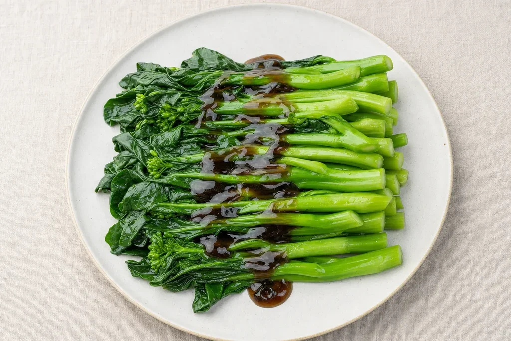 Steamed Chinese broccoli on a ceramic plate with a drizzle of thick glossy oyster sauce on linen surface