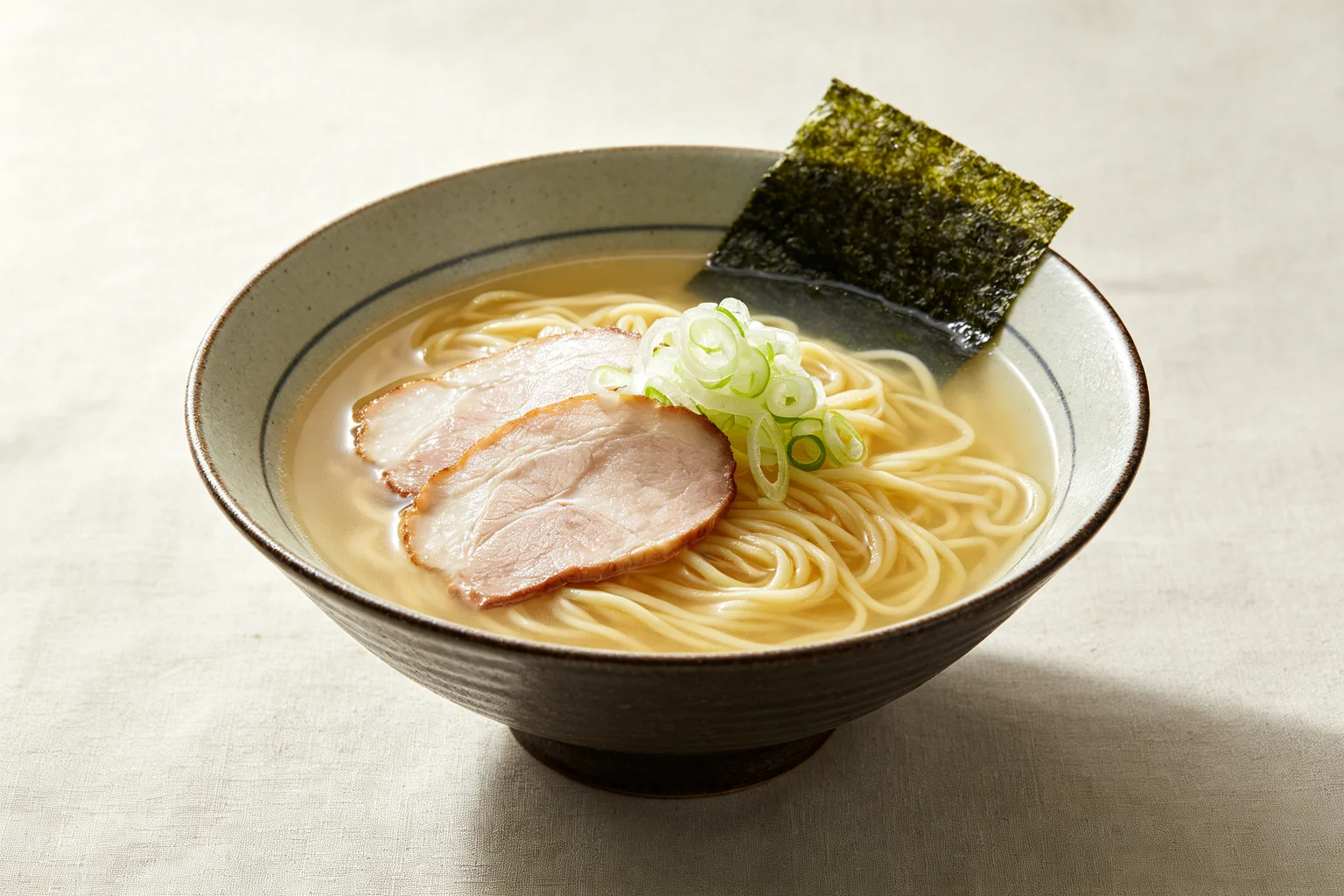  Bowl of shio ramen with pale golden almost-clear delicate  broth, straight noodles and minimal toppings on linen