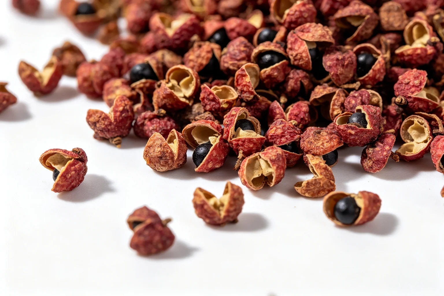  Extreme close-up macro shot of whole Sichuan peppercorns scattered on white surface showing the reddish-brown husks, split openings and black seeds inside