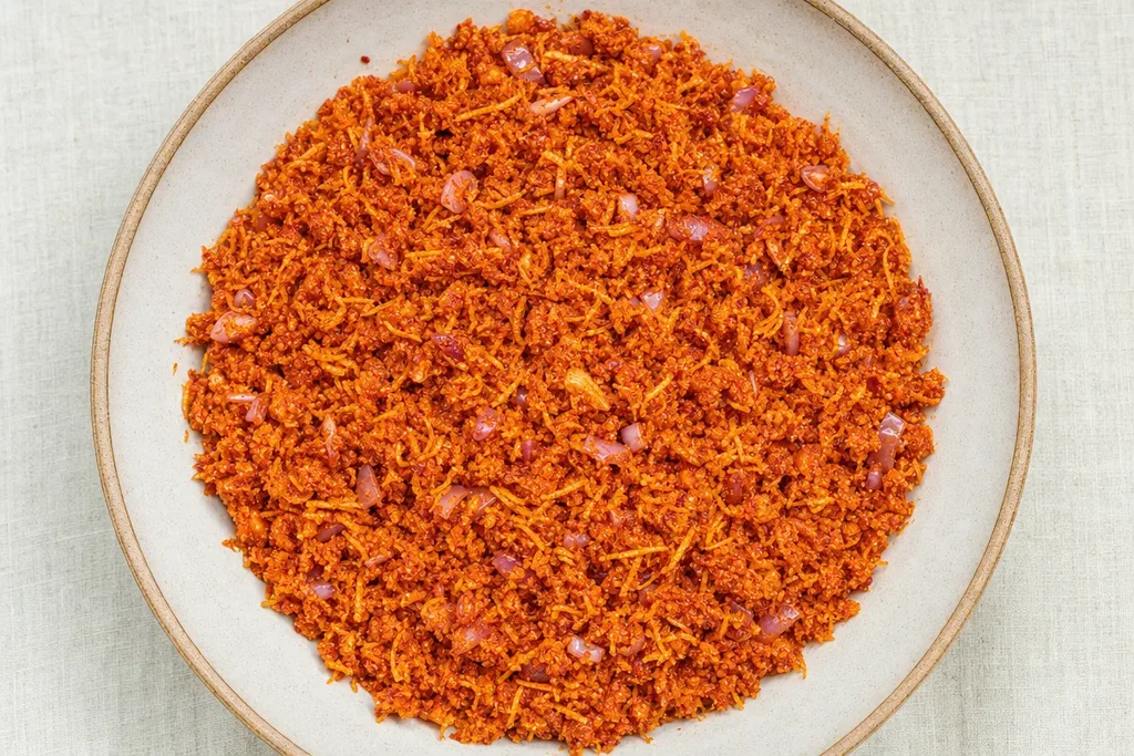 Freshly made Sri Lankan pol sambol in a ceramic bowl showing coarse red-orange coconut texture with shallots and chilli